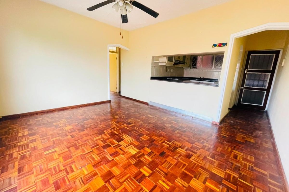 Spacious living area featuring traditional parquet flooring, a ceiling fan, and a convenient pass-through window connecting to the kitchen space.