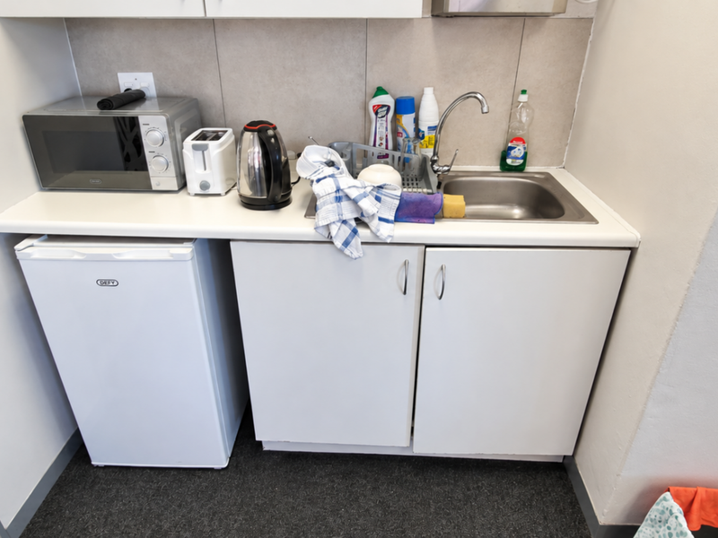 A compact office kitchenette featuring white cabinetry, a stainless steel sink, and a tiled backsplash, providing essential utility for a workspace.