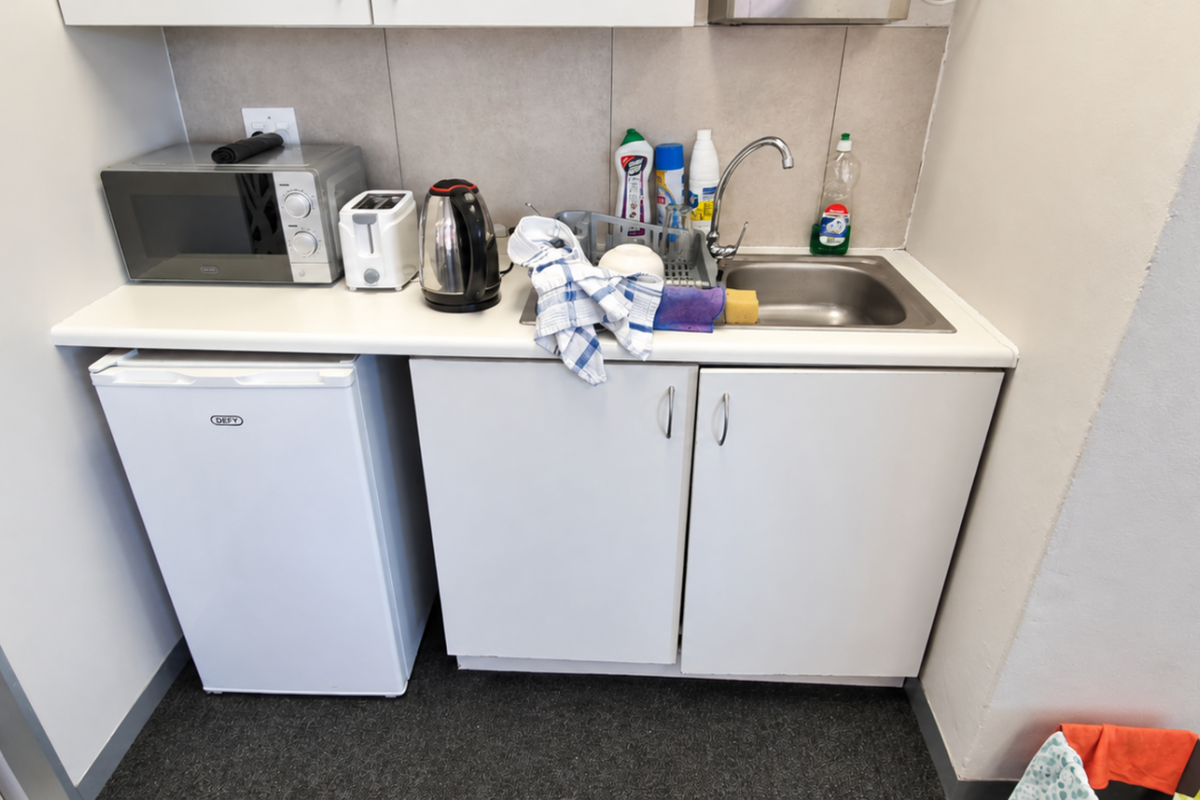 A compact office kitchenette featuring white cabinetry, a stainless steel sink, and a tiled backsplash, providing essential utility for a workspace.