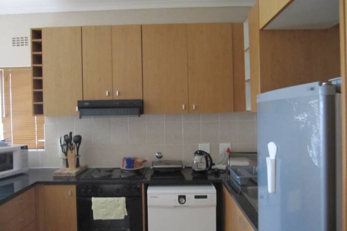 A functional kitchen featuring light wood-tone cabinetry, dark countertops, a tiled splashback, and integrated appliances including an oven, hob, and extractor fan.