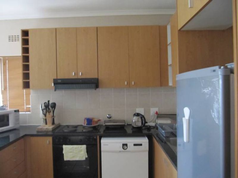 A functional kitchen featuring light wood-tone cabinetry, dark countertops, a tiled splashback, and integrated appliances including an oven, hob, and extractor fan.