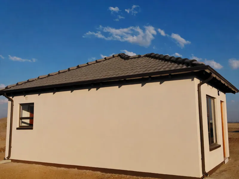 A view of the rear exterior of a modern house featuring a tiled roof, plastered walls, and aluminium window frames.