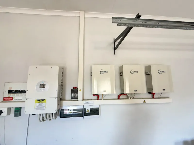 A clean utility wall featuring a solar inverter and multiple lithium-ion battery storage units, indicating a modern off-grid or backup power installation.