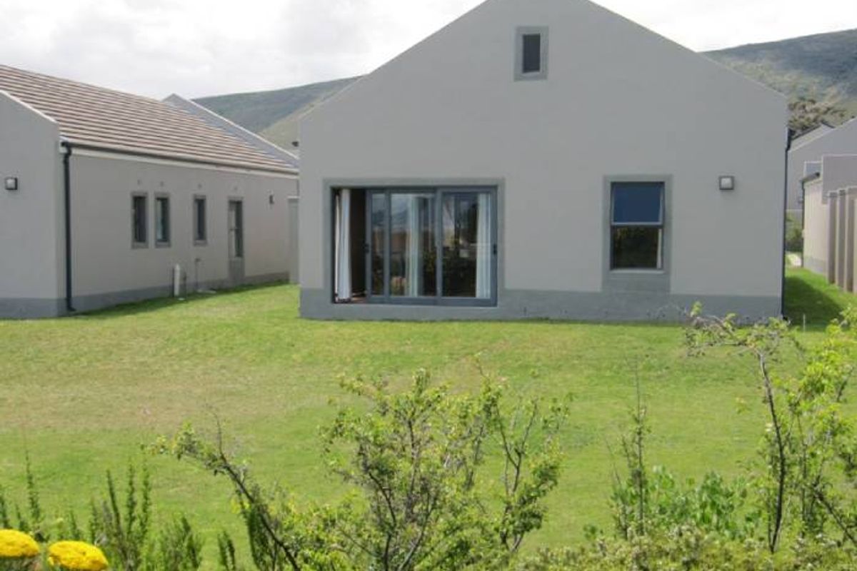 Rear view of a townhouse featuring a plastered facade, sliding glass doors, and a private lawn area.