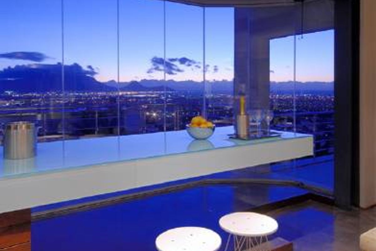 Modern interior space featuring a sleek glass-topped breakfast bar and expansive floor-to-ceiling windows offering panoramic city and mountain views.