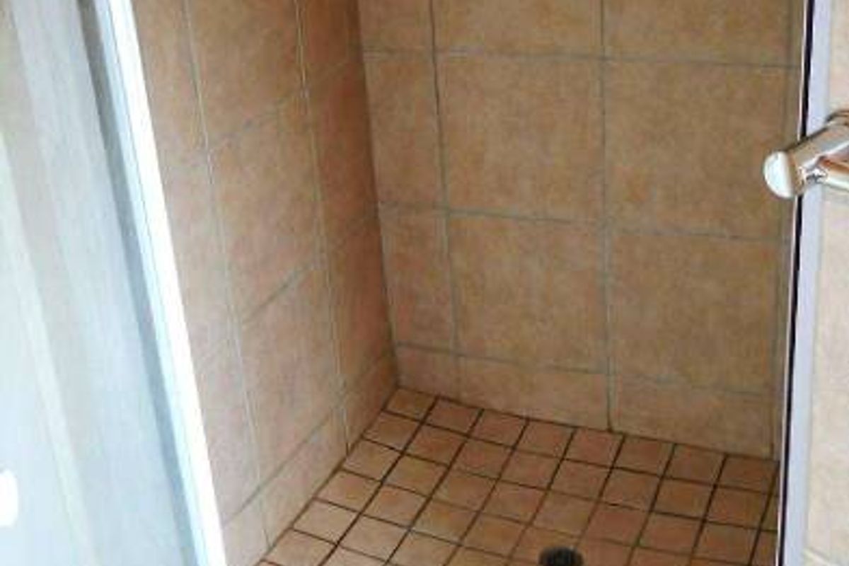 A functional shower stall featuring tiled walls and flooring with a glass enclosure, showing signs of wear consistent with age.