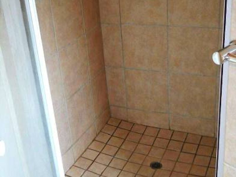 A functional shower stall featuring tiled walls and flooring with a glass enclosure, showing signs of wear consistent with age.