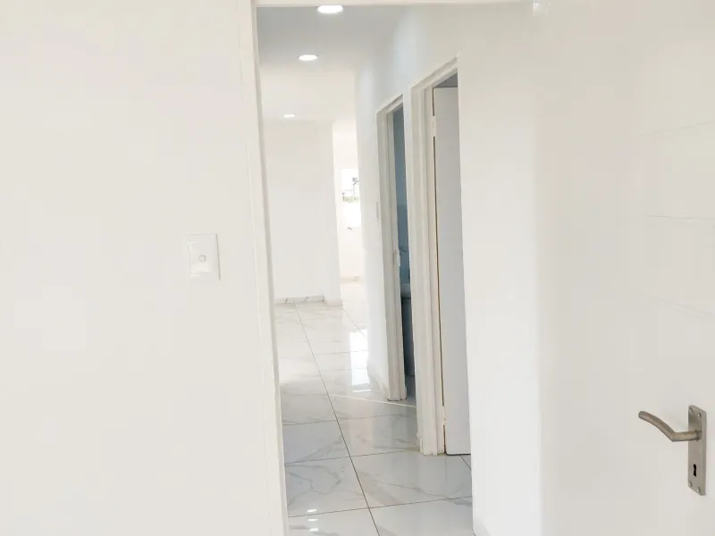 A bright, modern hallway featuring clean white walls and polished marble-look porcelain floor tiles, leading into an open-plan living area.