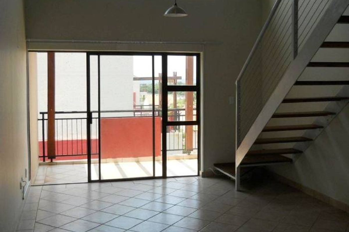 Spacious open-plan living area featuring tiled floors, a staircase with modern metal railings, and large sliding doors leading to an outdoor balcony.