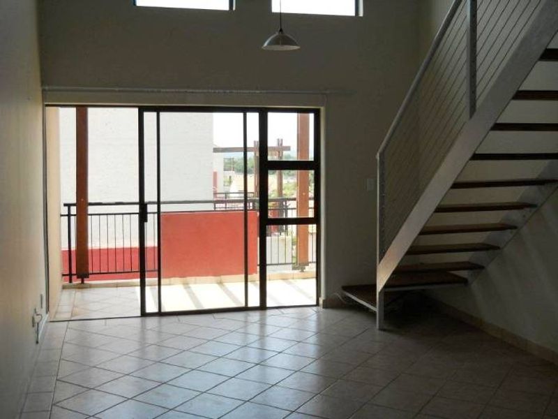 Spacious open-plan living area featuring tiled floors, a staircase with modern metal railings, and large sliding doors leading to an outdoor balcony.