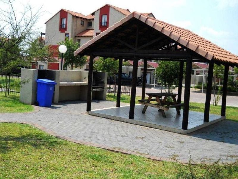 Outdoor communal entertainment area featuring a covered gazebo with a tiled floor and a built-in braai facility set within a landscaped garden.