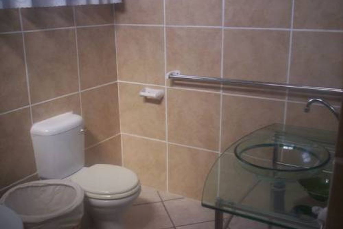 A functional bathroom featuring beige wall tiles, a glass vessel sink vanity, and a standard toilet with a wall-mounted grab rail.