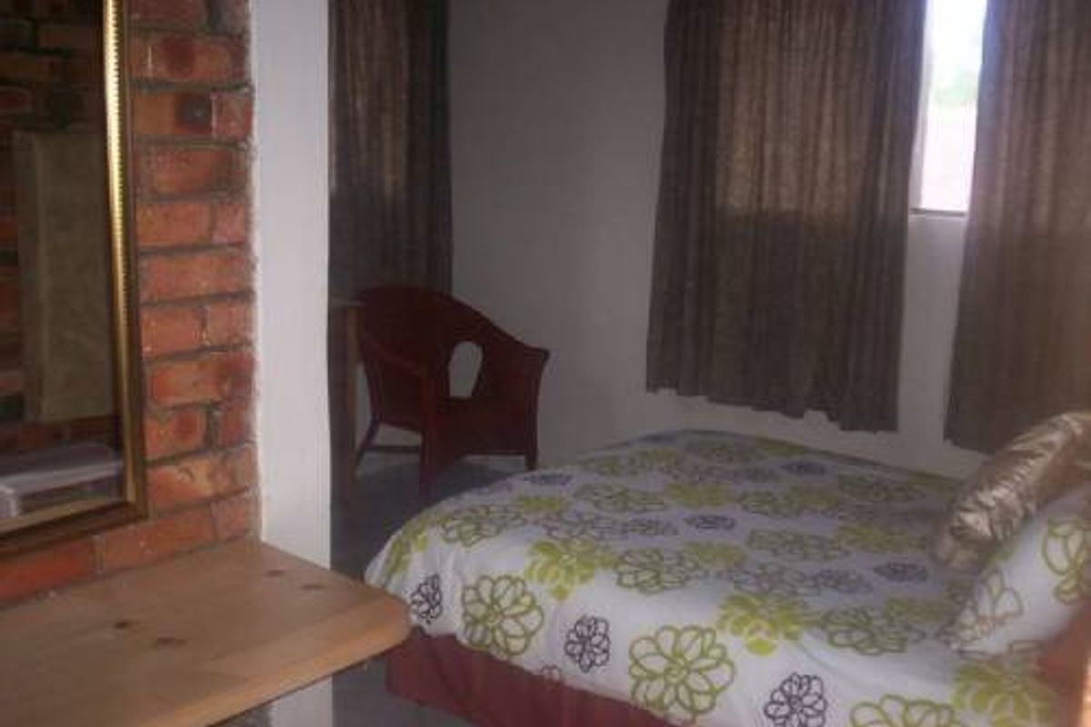 A bedroom featuring a rustic exposed brick wall accent and tiled flooring, providing a cozy and functional sleeping space.