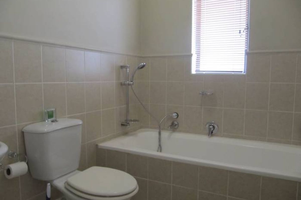 A functional bathroom featuring a built-in bathtub with shower mixer, a standard toilet, and neutral wall tiling.