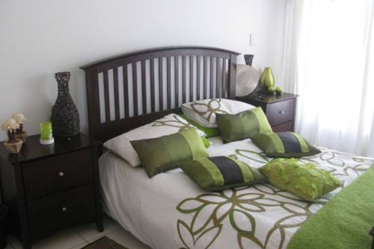 A well-lit bedroom featuring a dark wood headboard and neutral tiled flooring, offering a comfortable and functional sleeping space.