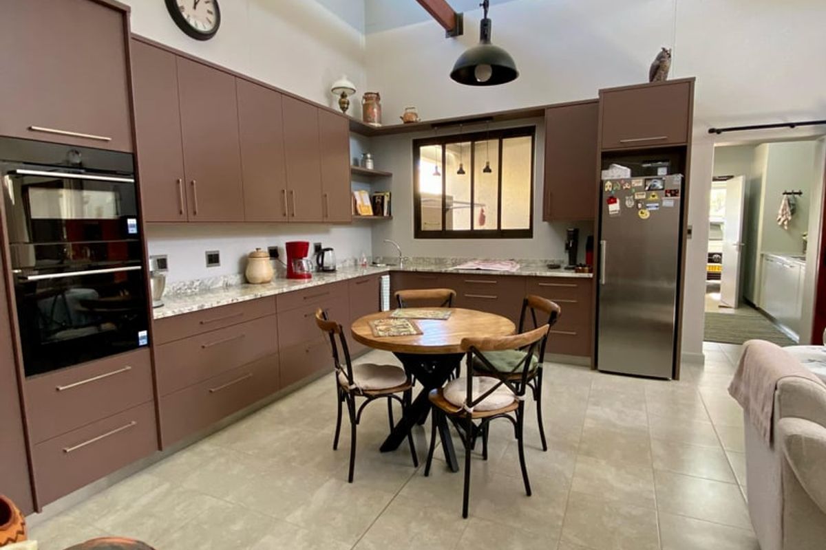 Spacious kitchen featuring modern brown cabinetry, stone countertops, high vaulted ceilings with exposed timber beams, and a large skylight for natural light.