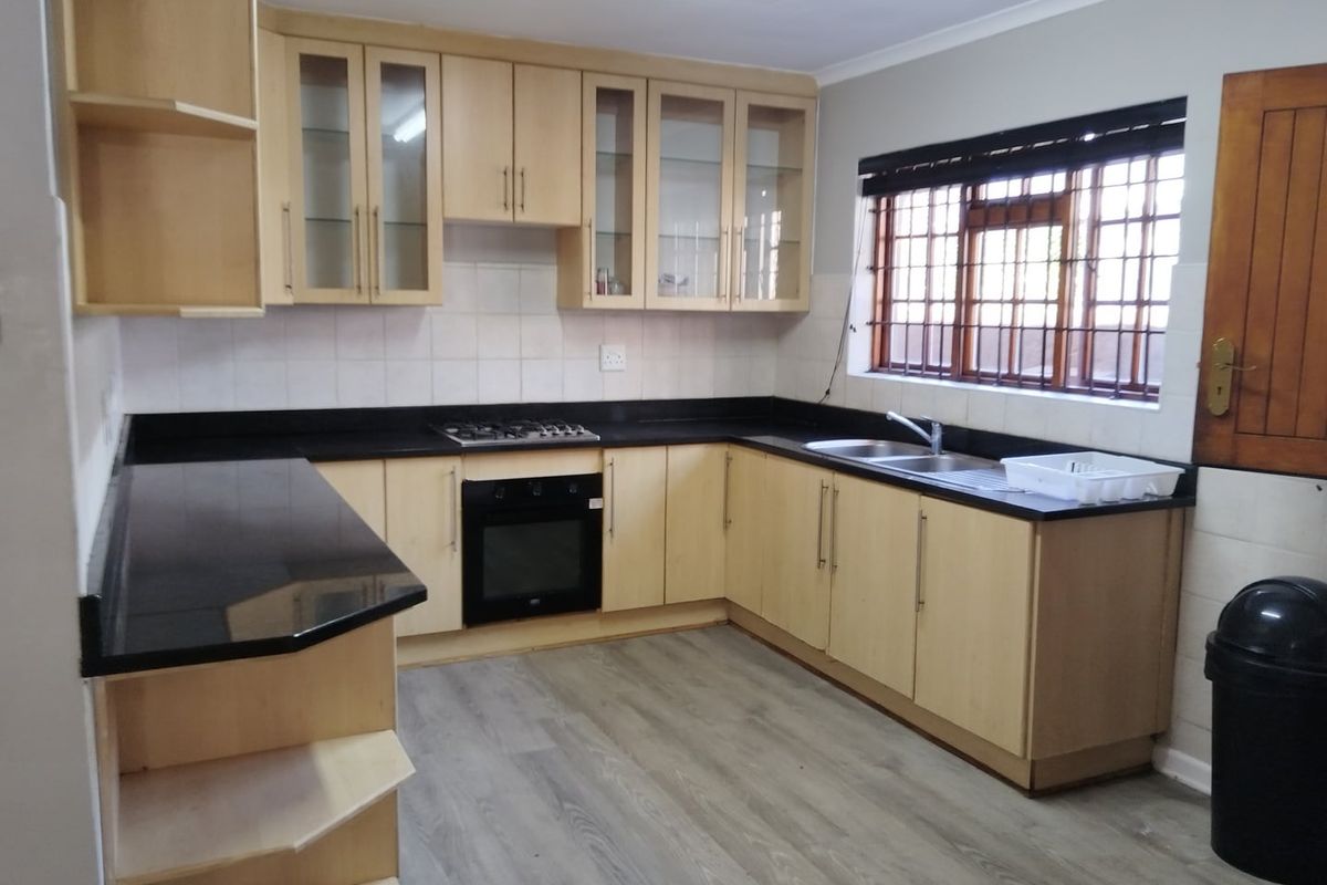 A functional kitchen featuring light wood cabinetry, black granite countertops, a gas hob, built-in oven, and durable laminate flooring.