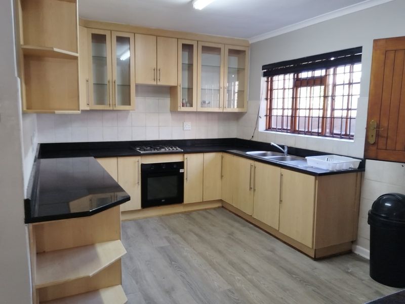 A functional kitchen featuring light wood cabinetry, black granite countertops, a gas hob, built-in oven, and durable laminate flooring.