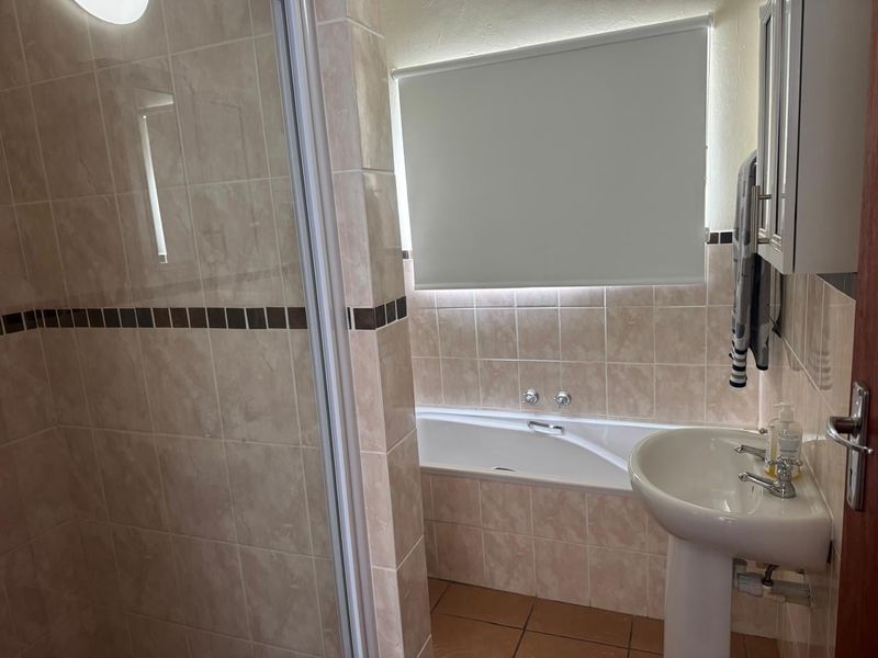A functional bathroom featuring a shower enclosure, bathtub, and pedestal basin with neutral wall and floor tiling.
