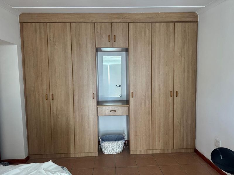 A bedroom featuring a large, light wood-grain built-in wardrobe with an integrated central vanity and mirror, complemented by tiled flooring.