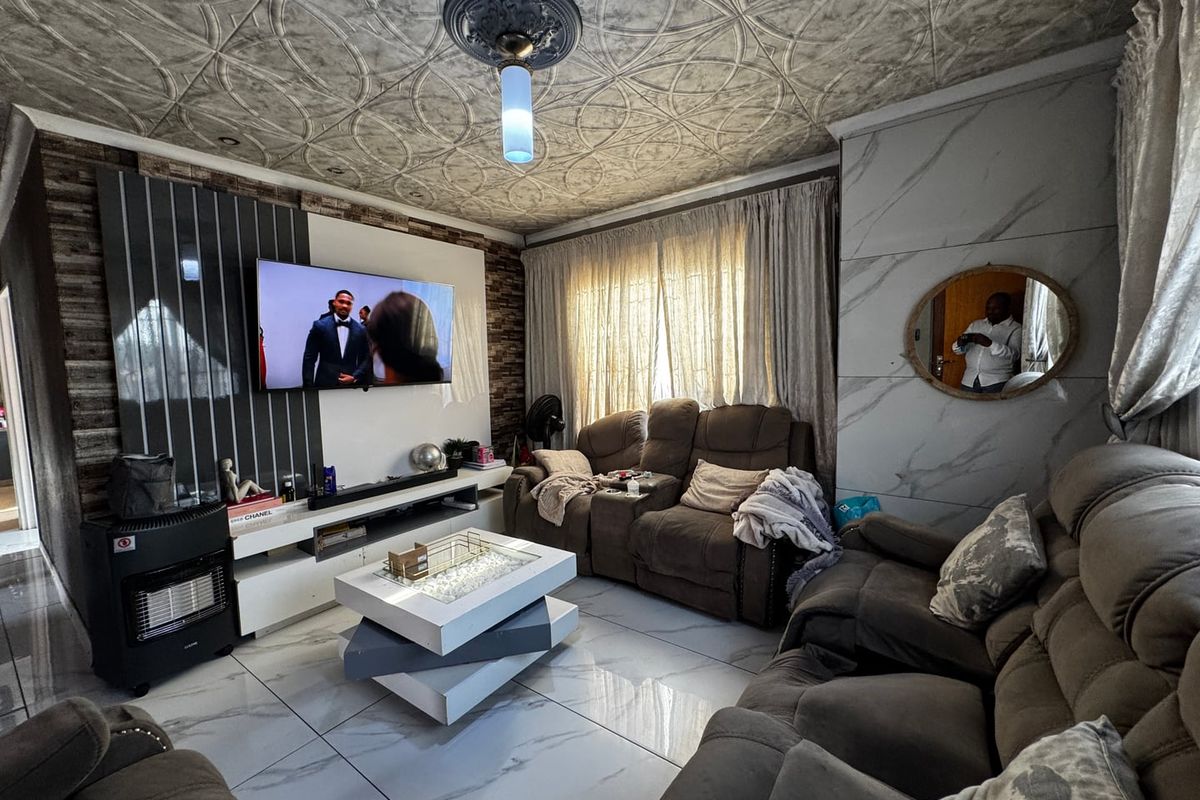 A living room featuring large format marble-look floor tiles, a decorative patterned ceiling, and a built-in media wall with integrated shelving.