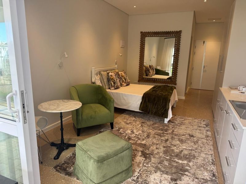 A modern open-plan studio apartment featuring a kitchenette, sleeping area, and direct access to an outdoor patio through a sliding glass door.