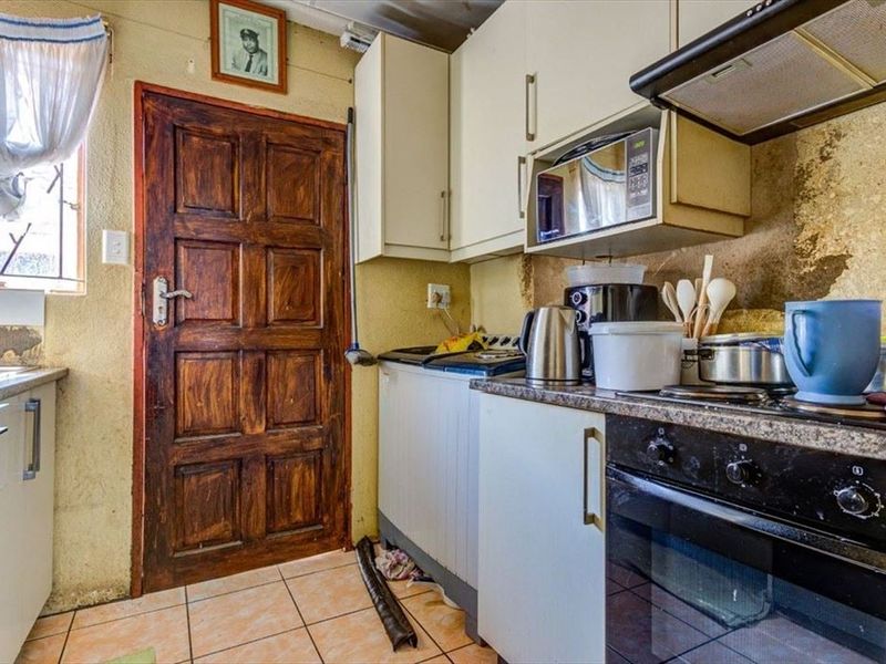 A compact kitchen featuring built-in cabinetry, an integrated oven, hob, and extractor fan, with visible wear to the wall finishes requiring maintenance.