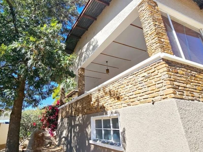 A covered balcony featuring stone cladding, exposed beam ceilings, and large glass sliding doors, offering an elevated outdoor living space.