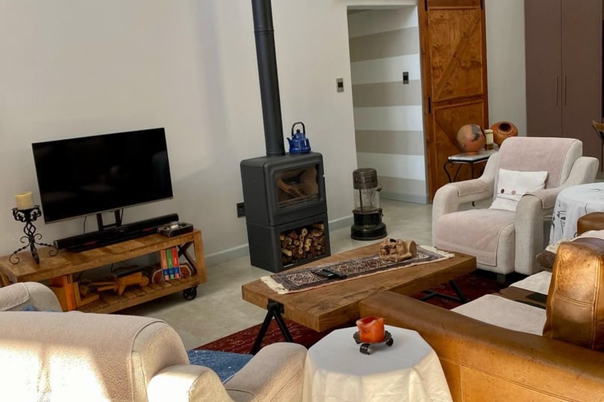A cozy living room featuring a prominent freestanding wood-burning fireplace, exposed timber ceiling beams, and a rustic sliding barn door.