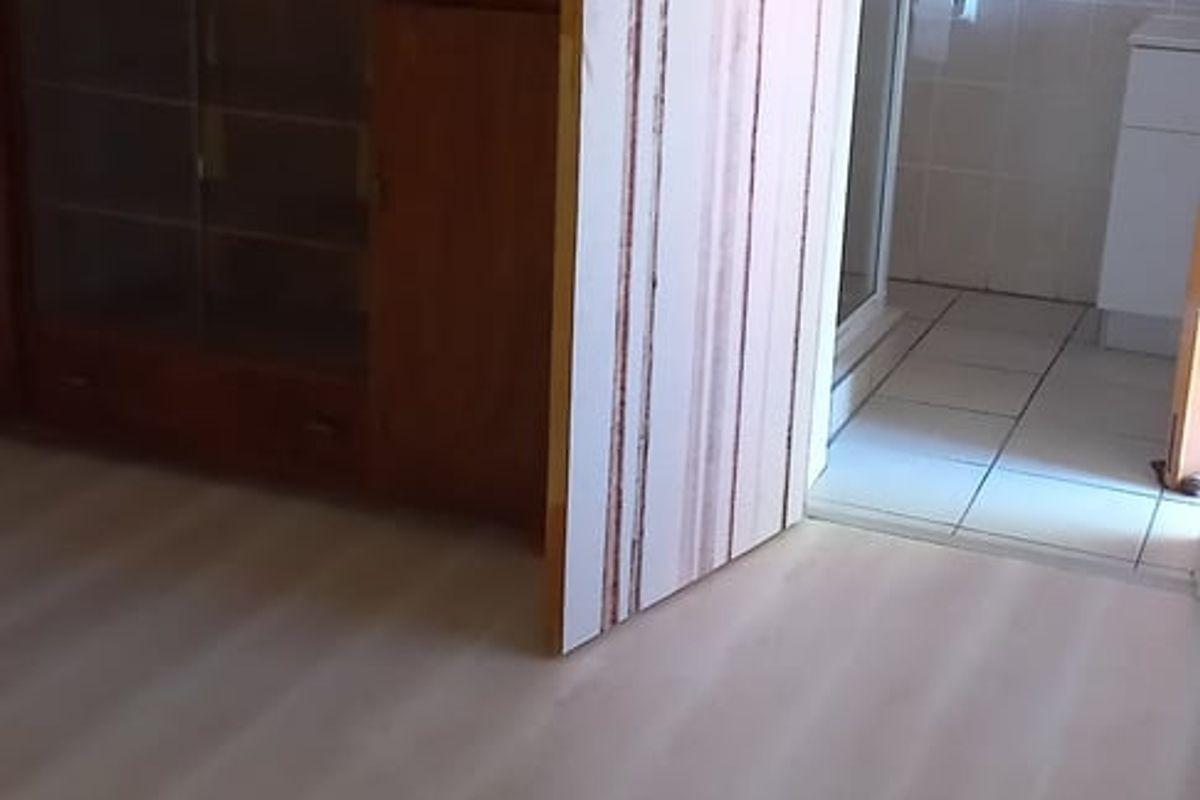 A bedroom featuring light-toned laminate flooring with direct access to an adjoining tiled bathroom.