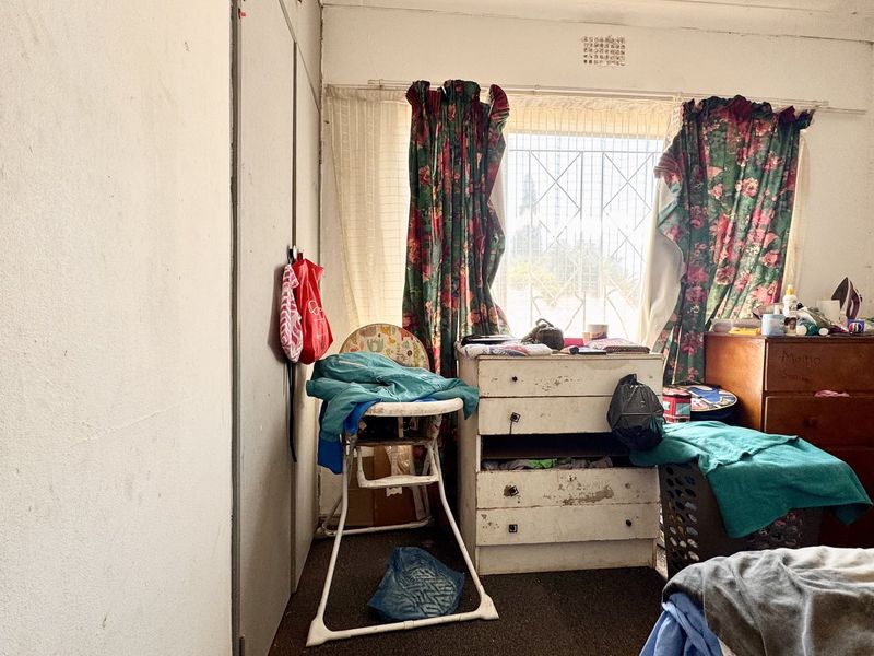 A bedroom featuring built-in cupboards and a window with security bars, requiring cosmetic updates to improve its overall condition and appeal.