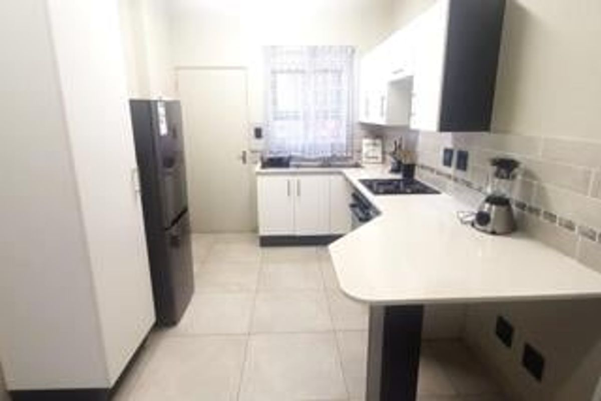 A modern kitchen featuring white cabinetry, stone countertops, a built-in hob, and tiled flooring with a clean, functional layout.
