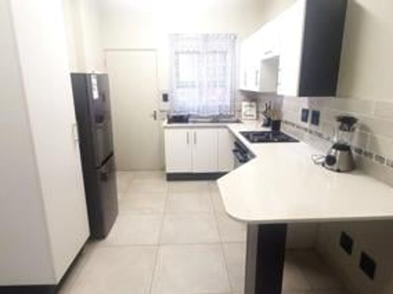 A modern kitchen featuring white cabinetry, stone countertops, a built-in hob, and tiled flooring with a clean, functional layout.