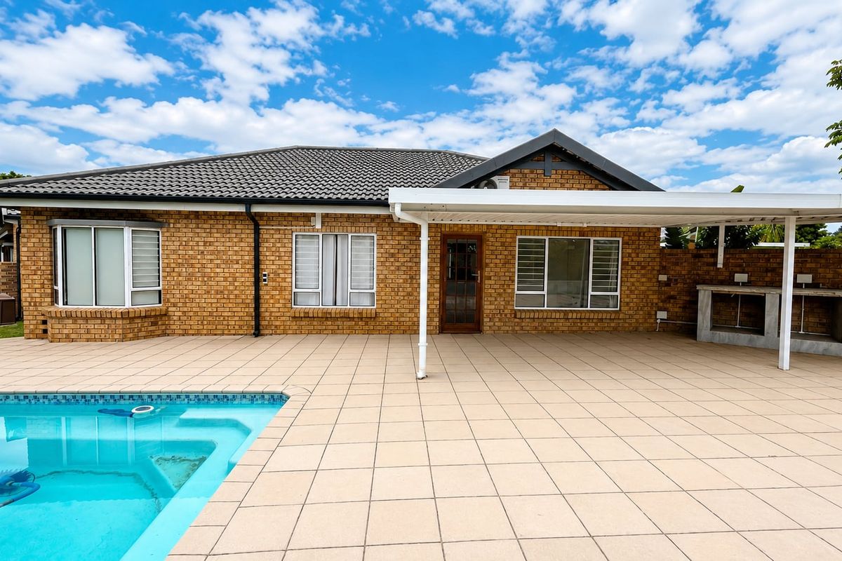 A spacious rear exterior featuring a paved patio, a built-in braai area, and a swimming pool set against a brick townhouse facade.