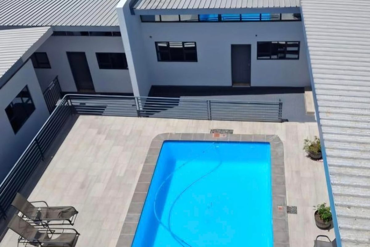 Aerial view of a guest house courtyard featuring a rectangular swimming pool, tiled patio area, and modern metal roofing structures.