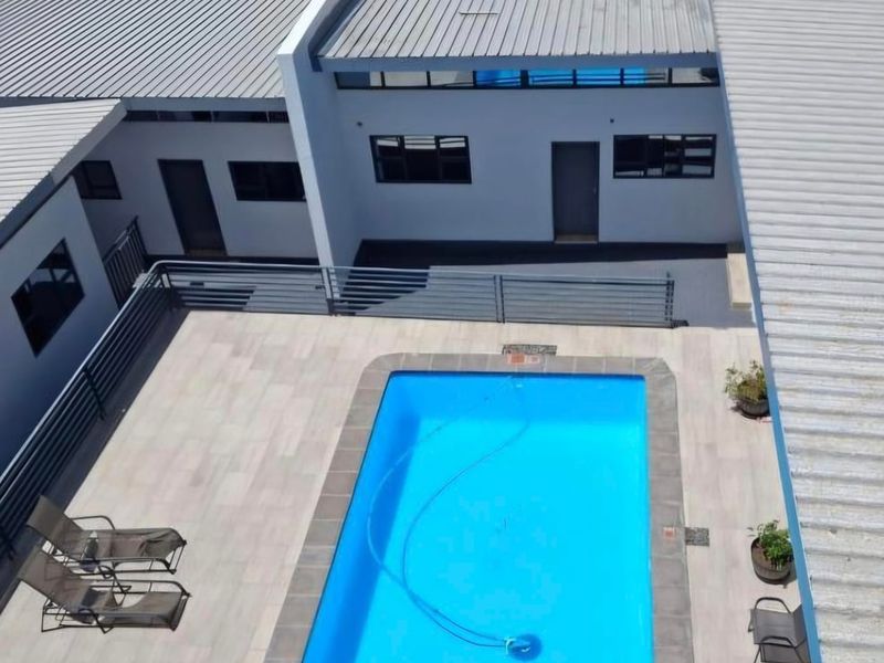 Aerial view of a guest house courtyard featuring a rectangular swimming pool, tiled patio area, and modern metal roofing structures.