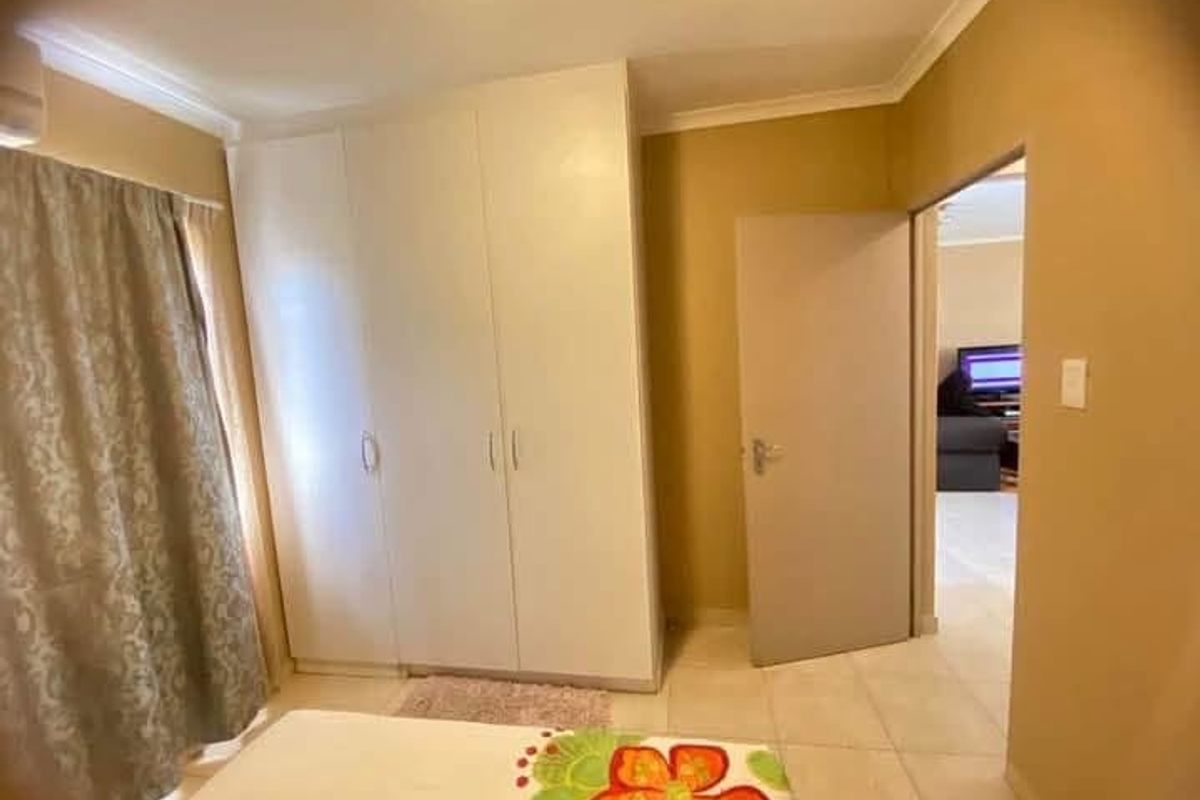 A bedroom featuring built-in cupboards, tiled flooring, and coved ceiling details, with an open doorway leading to an adjacent living area.
