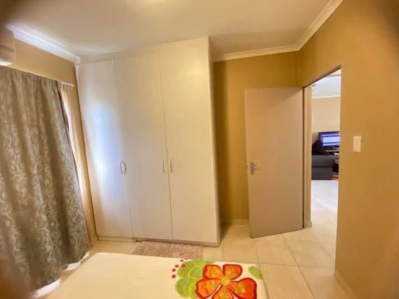 A bedroom featuring built-in cupboards, tiled flooring, and coved ceiling details, with an open doorway leading to an adjacent living area.