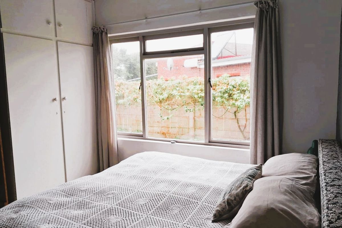 A bedroom featuring built-in cupboards and a large window with views of the rear garden area.