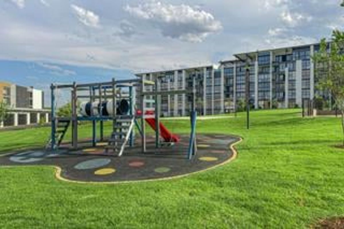 Communal outdoor area featuring a well-maintained lawn and a modern playground structure set against the apartment building facade.