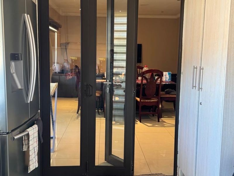 A functional kitchen area featuring modern built-in cabinetry and tiled flooring, with a glass-paneled door providing a clear view into the adjacent dining space.