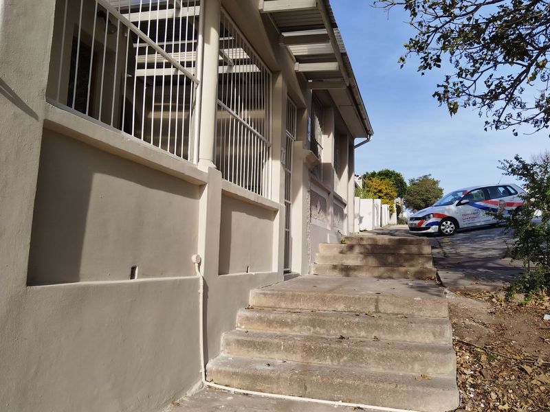 Exterior view of the property entrance featuring concrete stairs and security bars on the windows.