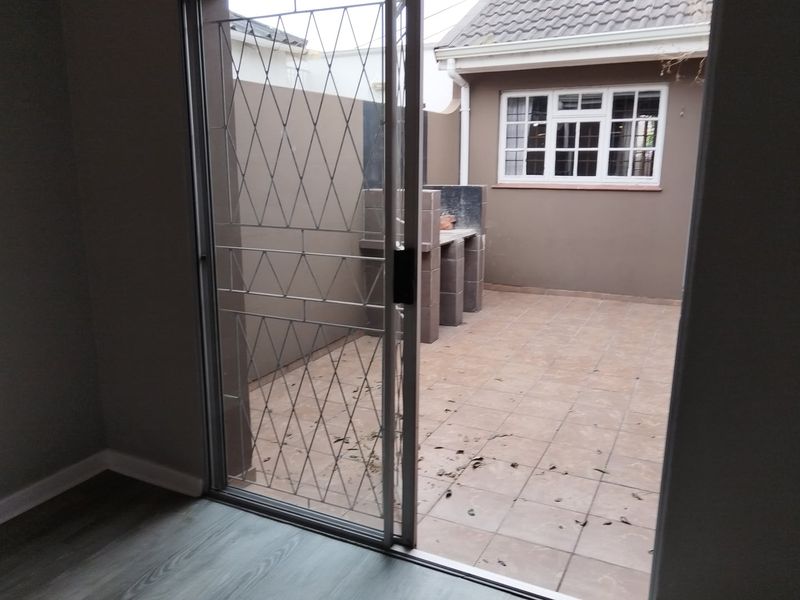 A private outdoor patio area featuring tiled flooring, a built-in braai, and secure sliding door access, perfect for outdoor entertaining.