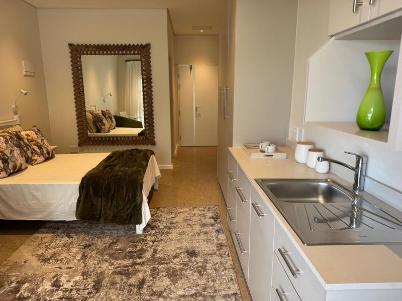 An open-plan studio unit featuring a compact kitchenette with stone countertops, stainless steel sink, and built-in cabinetry, seamlessly integrated with the bedroom area.