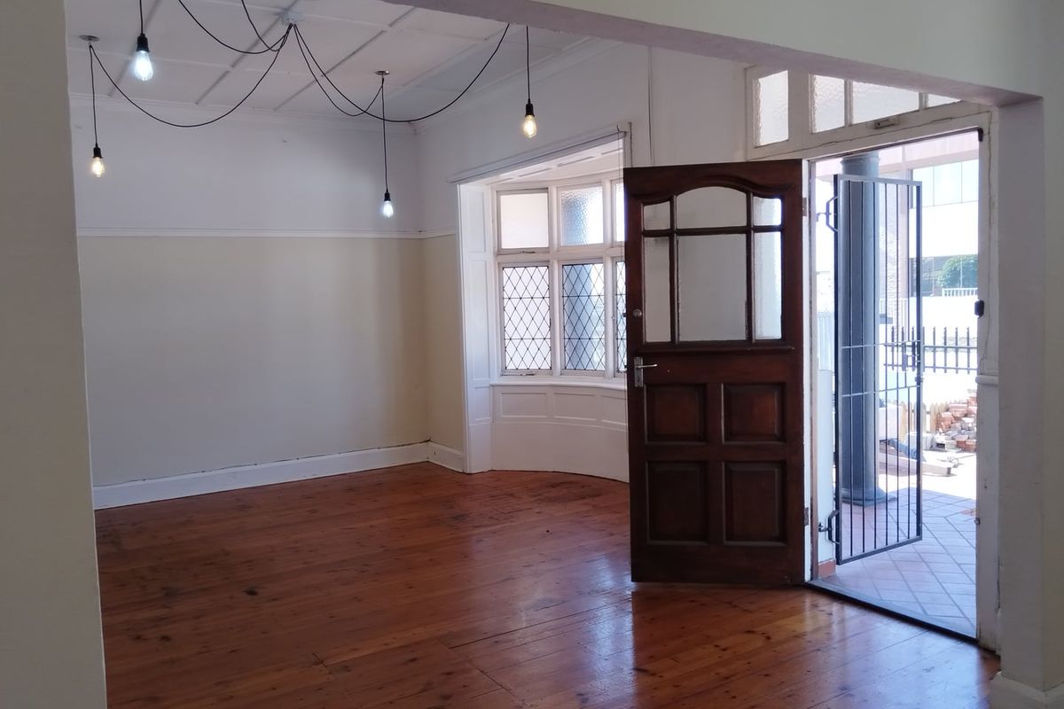 Spacious living area featuring polished hardwood flooring, a classic bay window with leaded glass, and direct access to an outdoor patio area.