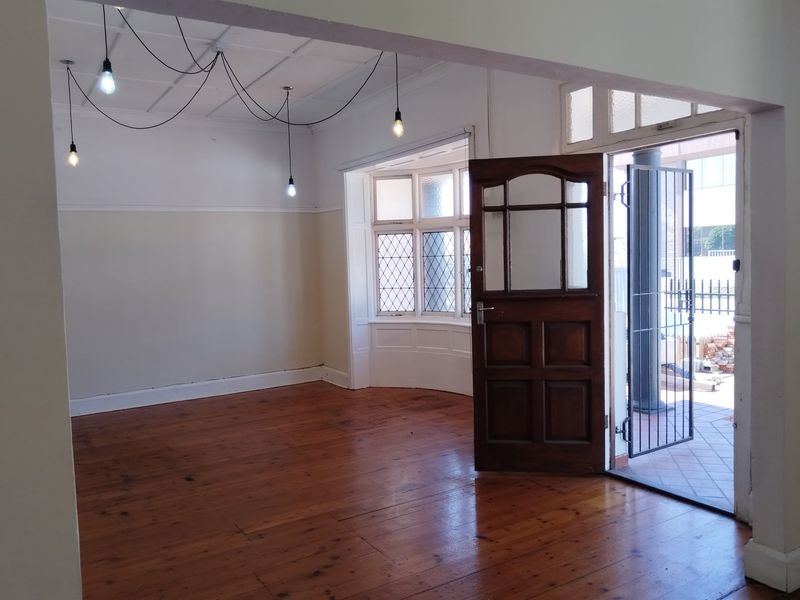 Spacious living area featuring polished hardwood flooring, a classic bay window with leaded glass, and direct access to an outdoor patio area.