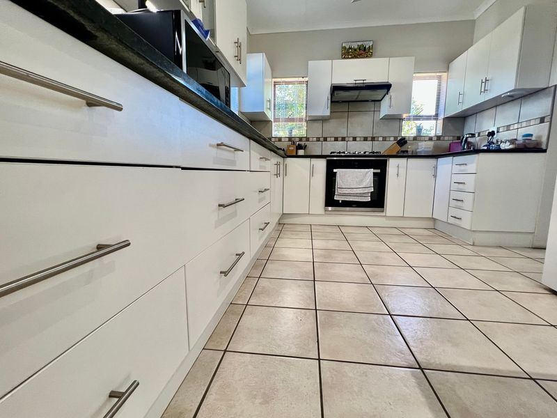 A well-maintained kitchen featuring white cabinetry, dark stone countertops, tiled flooring, and integrated appliances including an oven, hob, and extractor fan.