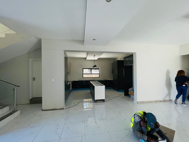 Spacious open-plan kitchen area featuring modern cabinetry, a central island, and polished porcelain tiles, currently undergoing final finishing touches.