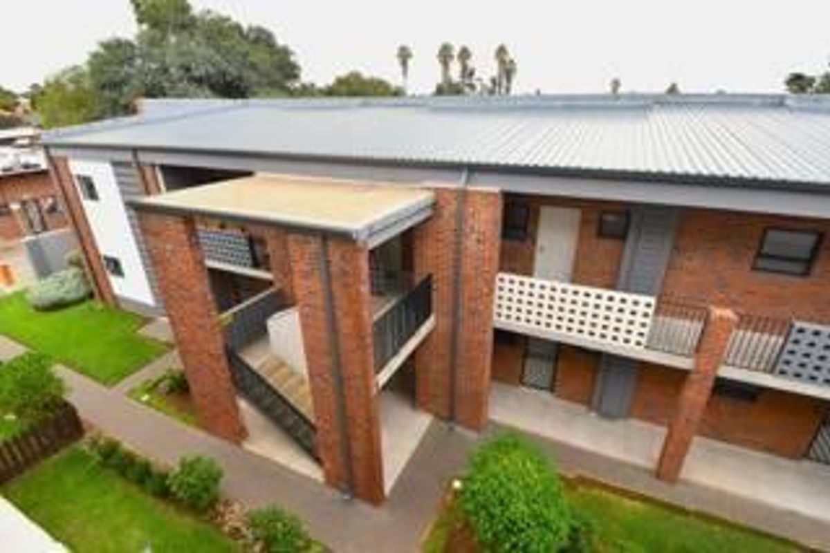 An elevated view of an apartment building exterior featuring brick construction, metal roofing, and external staircases with paved walkways and landscaped grounds.