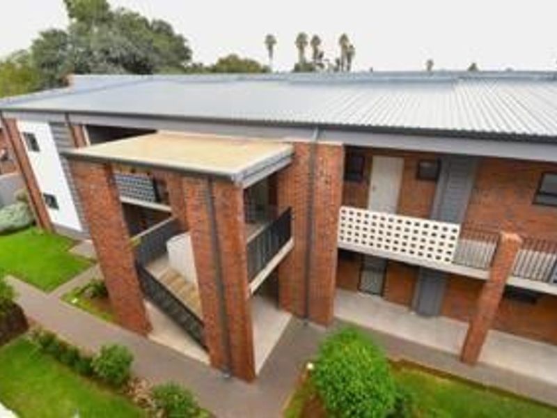 An elevated view of an apartment building exterior featuring brick construction, metal roofing, and external staircases with paved walkways and landscaped grounds.